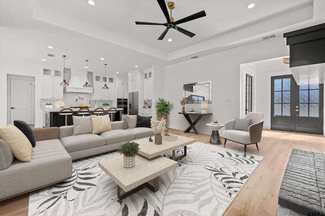 living room featuring a tray ceiling, ceiling fan, french doors, and light hardwood / wood-style floors