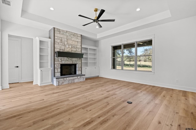 unfurnished living room with built in shelves, ceiling fan, a fireplace, and a tray ceiling