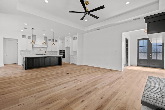 unfurnished living room with ceiling fan, light hardwood / wood-style floors, french doors, and a tray ceiling