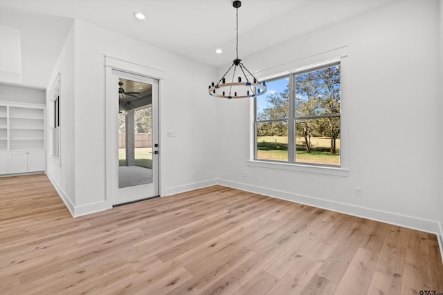 unfurnished dining area with light wood-type flooring, an inviting chandelier, built in features, and plenty of natural light