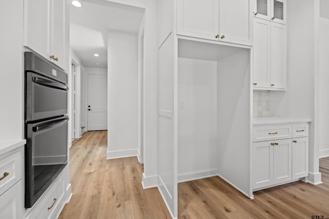 kitchen with light hardwood / wood-style flooring, tasteful backsplash, white cabinetry, and black double oven