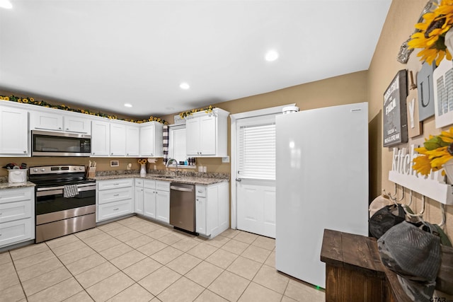 kitchen featuring sink, light tile patterned floors, appliances with stainless steel finishes, light stone counters, and white cabinetry