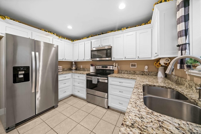 kitchen featuring sink, light tile patterned floors, light stone counters, white cabinets, and appliances with stainless steel finishes