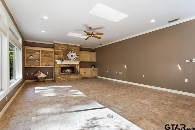 unfurnished living room featuring a brick fireplace, ceiling fan, ornamental molding, and a skylight