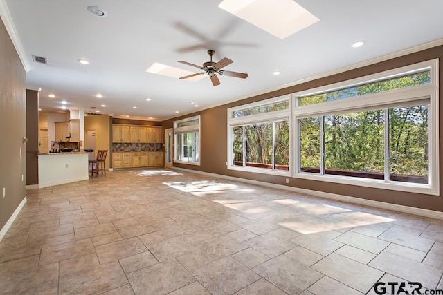 unfurnished living room with a skylight, crown molding, and ceiling fan