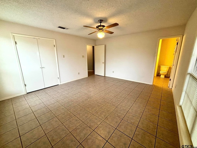 unfurnished bedroom featuring ensuite bath, tile patterned flooring, ceiling fan, a textured ceiling, and a closet