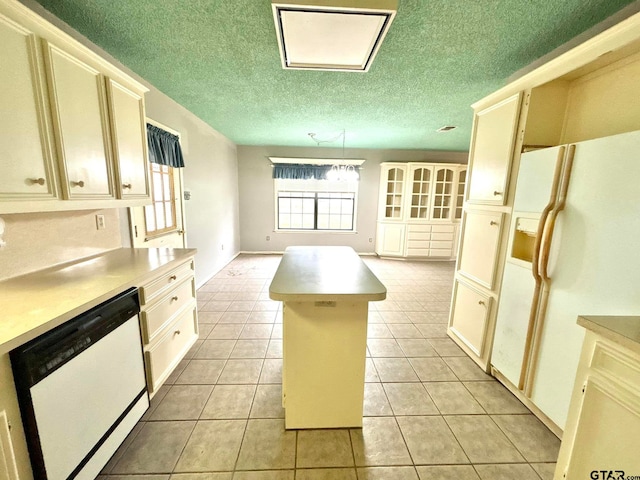 kitchen featuring white appliances, a textured ceiling, cream cabinets, light tile patterned floors, and a center island