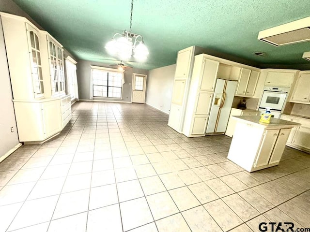 kitchen featuring white appliances, ceiling fan with notable chandelier, hanging light fixtures, a textured ceiling, and a kitchen island