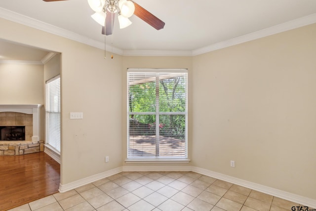 empty room with light tile patterned floors, baseboards, ceiling fan, a fireplace, and crown molding