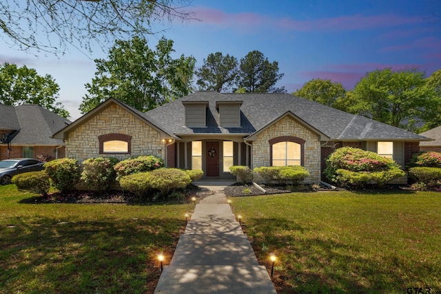 view of front of home featuring roof with shingles, stone siding, and a lawn