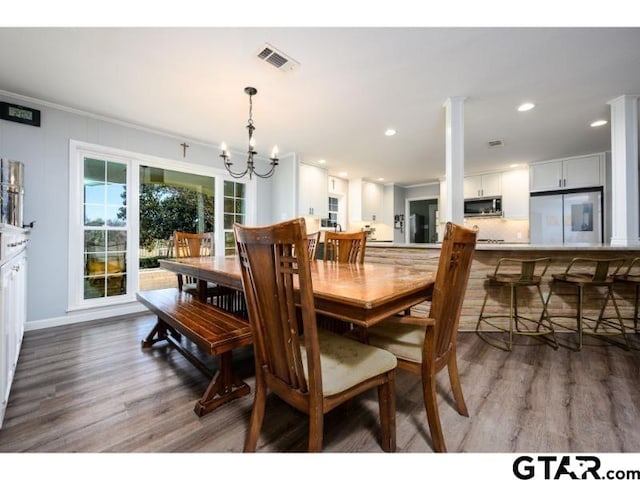 dining room with ornamental molding, a notable chandelier, hardwood / wood-style floors, and ornate columns