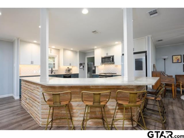 kitchen with appliances with stainless steel finishes, dark wood-type flooring, white cabinets, and a breakfast bar area