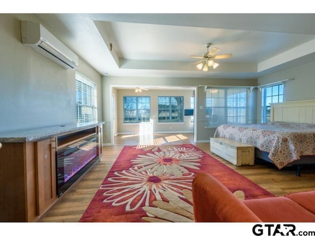 bedroom featuring a wall unit AC, ceiling fan, a tray ceiling, and light wood-type flooring