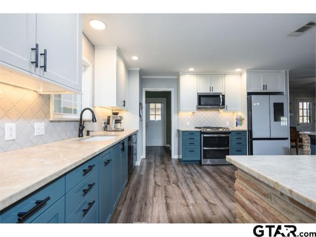 kitchen featuring appliances with stainless steel finishes, blue cabinetry, hardwood / wood-style flooring, sink, and white cabinetry