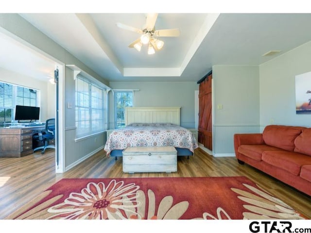 bedroom with ceiling fan, light wood-type flooring, and a tray ceiling