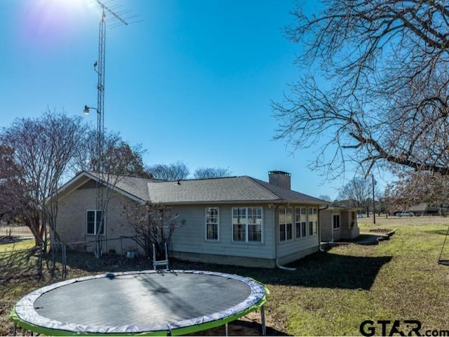 back of house with a lawn and a trampoline