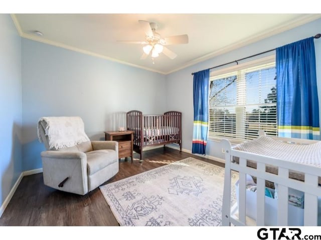 bedroom with ceiling fan, dark hardwood / wood-style flooring, a crib, and crown molding