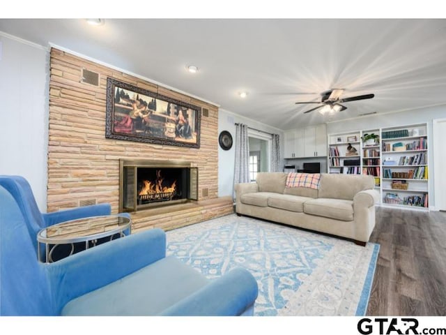 living room featuring ornamental molding, ceiling fan, a stone fireplace, and wood-type flooring