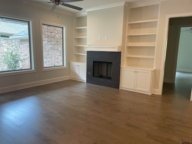 unfurnished living room with built in shelves, ceiling fan, crown molding, a fireplace, and dark hardwood / wood-style floors