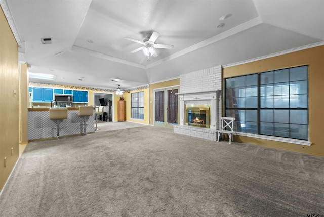 unfurnished living room with ceiling fan, a tray ceiling, ornamental molding, and a fireplace