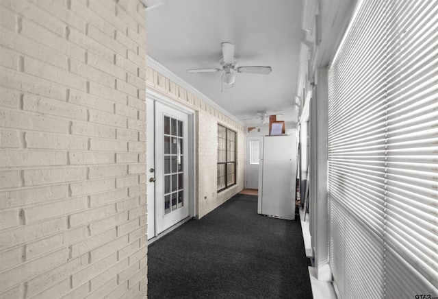 hallway with ornamental molding, dark colored carpet, and brick wall