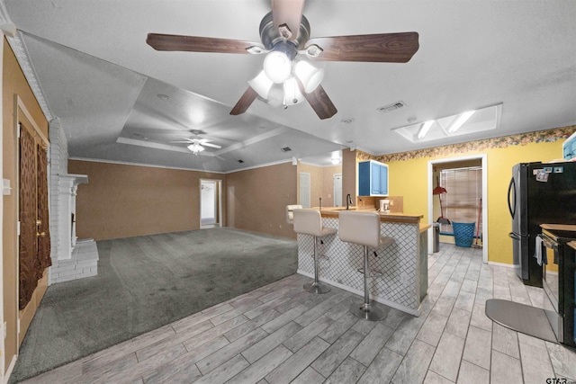 kitchen featuring light colored carpet, kitchen peninsula, stainless steel range with electric stovetop, a kitchen breakfast bar, and ceiling fan