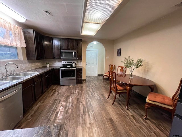 kitchen with stainless steel appliances, hardwood / wood-style flooring, dark brown cabinetry, sink, and decorative backsplash