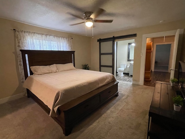 carpeted bedroom featuring a barn door, ceiling fan, connected bathroom, and a textured ceiling