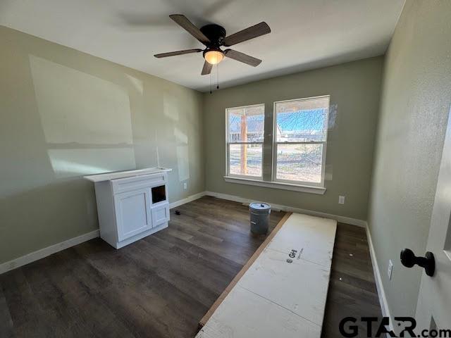 interior space featuring a ceiling fan, baseboards, and dark wood-style flooring