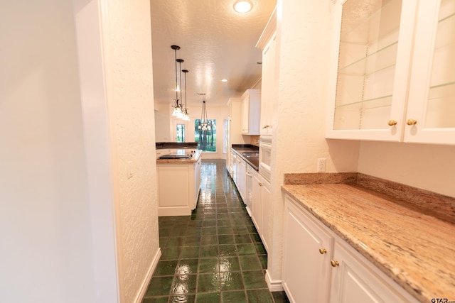 kitchen with hanging light fixtures, a textured ceiling, light stone counters, and white cabinets