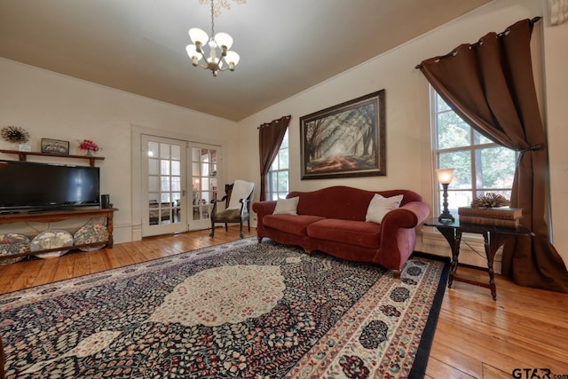 living room featuring lofted ceiling, light hardwood / wood-style flooring, a notable chandelier, and french doors