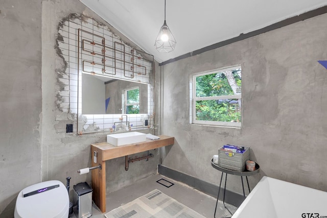 bathroom featuring sink, a tub to relax in, concrete flooring, lofted ceiling, and toilet