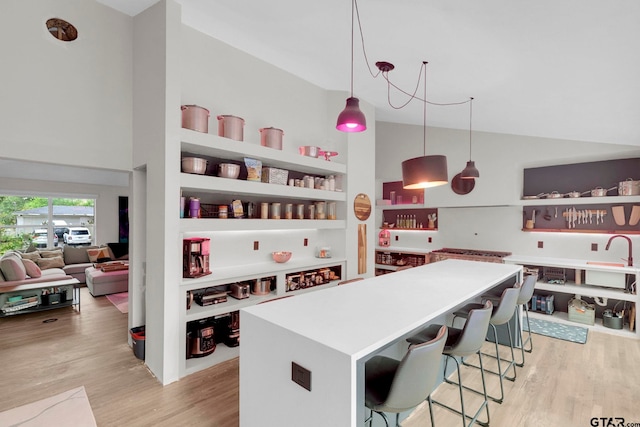 kitchen featuring a center island, a kitchen breakfast bar, light hardwood / wood-style flooring, high vaulted ceiling, and pendant lighting