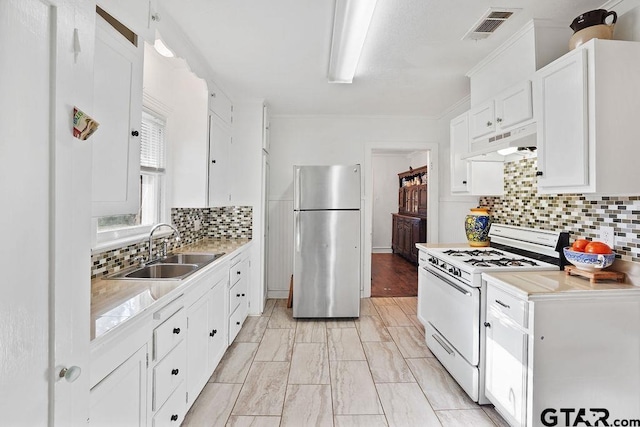 818 Rusk St, Tyler, TX 75701 - kitchen featuring freestanding refrigerator, white range with gas stovetop, under cabinet range hood, white cabinets, and backsplash
