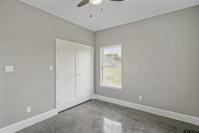 unfurnished bedroom with finished concrete flooring, a closet, a ceiling fan, and baseboards