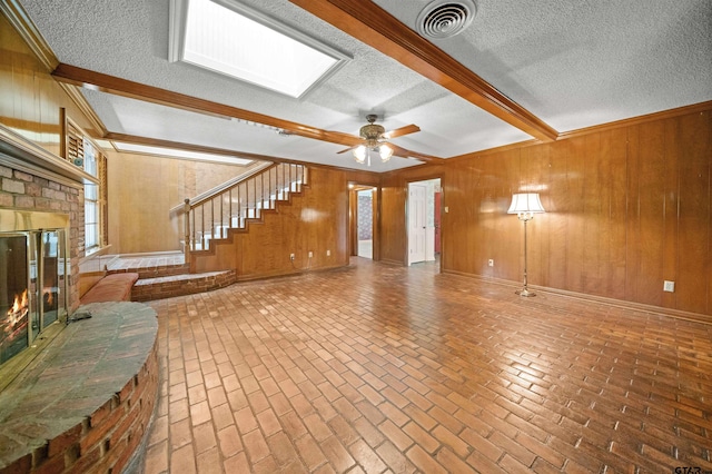 1101 Canada St, Jacksonville, TX 75766 - unfurnished living room featuring a fireplace, wood walls, brick flooring, a textured ceiling, and stairs