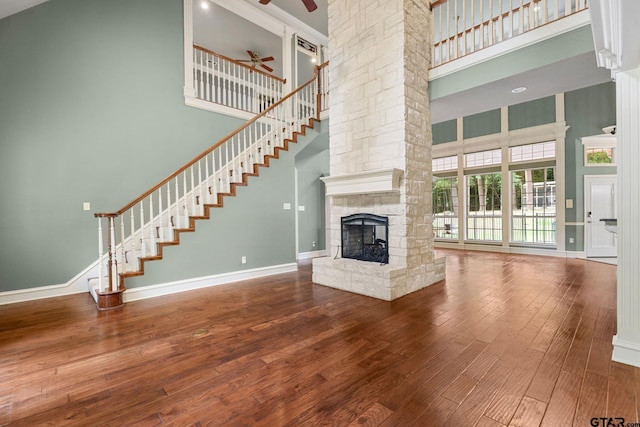801 Wilder Way, Tyler, TX 75703 - unfurnished living room with a towering ceiling, a ceiling fan, a stone fireplace, hardwood / wood-style flooring, and ornate columns