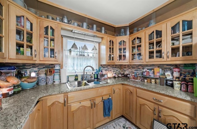 kitchen featuring a sink, glass insert cabinets, light stone countertops, and backsplash