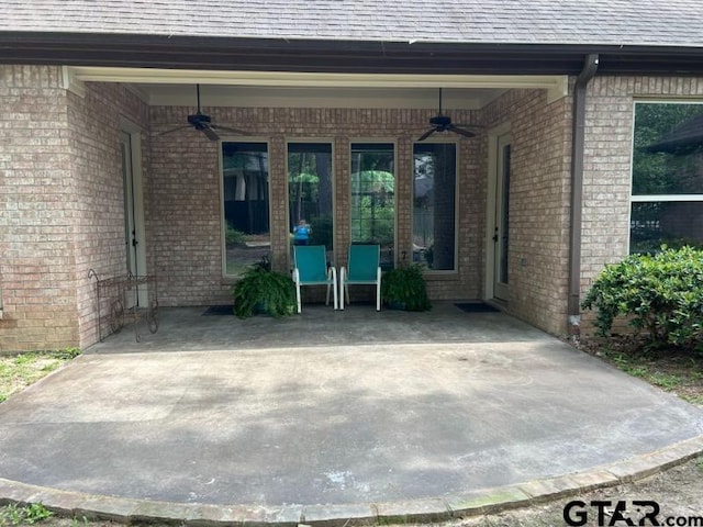 property entrance with ceiling fan, roof with shingles, brick siding, and a patio area
