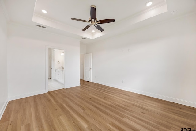 unfurnished bedroom featuring ceiling fan, light hardwood / wood-style flooring, ensuite bathroom, and a tray ceiling