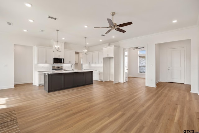 kitchen featuring hanging light fixtures, light hardwood / wood-style floors, a kitchen island with sink, white cabinets, and appliances with stainless steel finishes