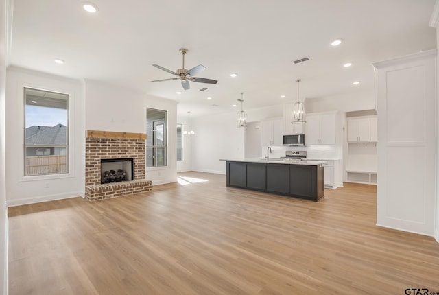 kitchen with white cabinetry, ceiling fan, stainless steel appliances, a brick fireplace, and a center island with sink