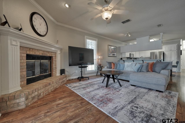 living room featuring crown molding, light hardwood / wood-style flooring, ceiling fan, a fireplace, and a textured ceiling