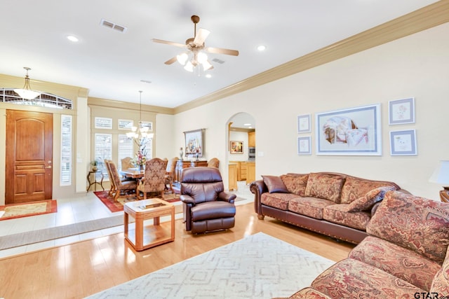 living room featuring wood finished floors, visible vents, arched walkways, crown molding, and ceiling fan with notable chandelier