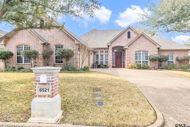 french country style house featuring driveway, brick siding, and a front yard