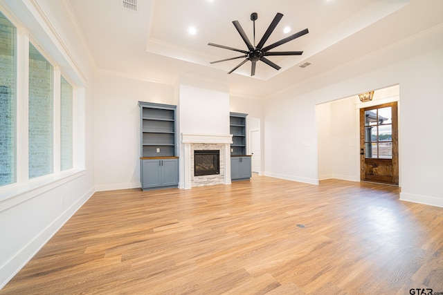 unfurnished living room with a raised ceiling, a ceiling fan, crown molding, light wood-type flooring, and a fireplace