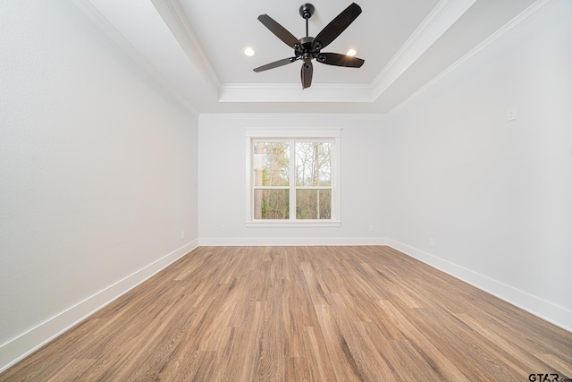 empty room featuring a raised ceiling, crown molding, light wood-style flooring, and baseboards