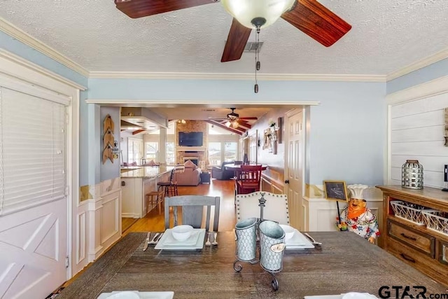 dining room with a ceiling fan, a fireplace, crown molding, and wood finished floors