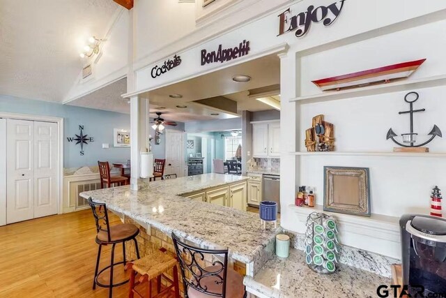 kitchen with a ceiling fan, a kitchen bar, light wood-style flooring, and light stone countertops