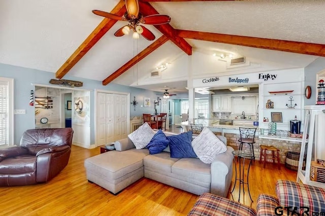 living area featuring a ceiling fan, visible vents, vaulted ceiling with beams, and light wood finished floors